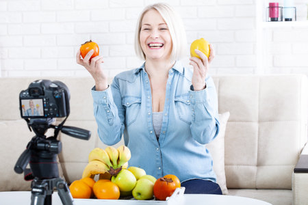 Happy woman expert nutritionist shows fruits to the camera at home.の写真素材