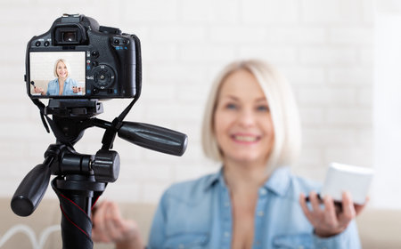 Woman doing makeup demonstrating cosmetics and shooting herself on video camera at home. Selective focusの写真素材