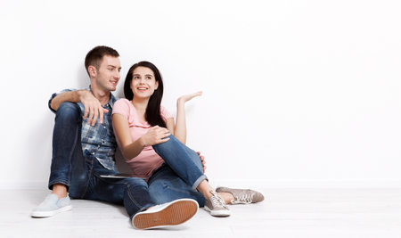 Happy young couple sitting on floor looking up while dreaming their new home and furnishing. Mock up for design.の写真素材