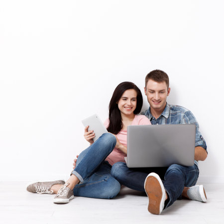 Happy young couple sitting on the floor with a laptop looking for their new home and furniture. Mock up for design.の写真素材