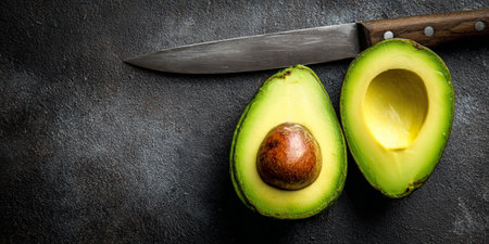 Halves of avocado with knife on black background. Top view.の素材