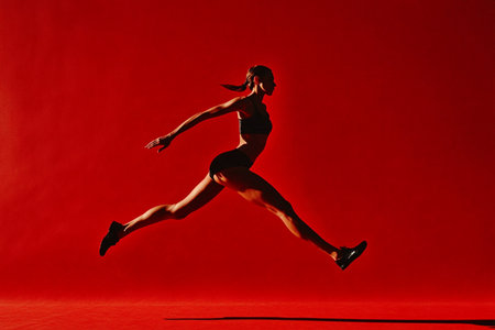 Silhouette of beautiful young woman in black sportswear running on red backgroundの素材