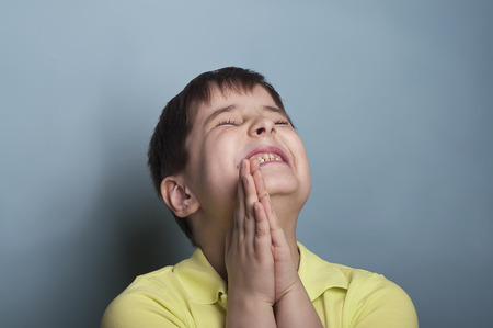 Extremely emotional portrait of a boy of seven in stress, asking for something. Studio shot on blueの写真素材