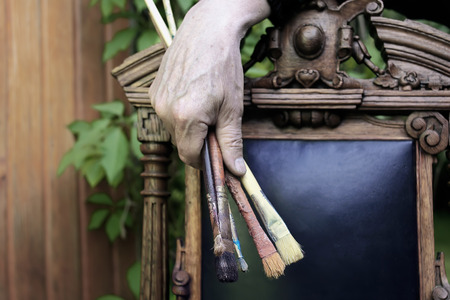 Hand of an artist holding brushes, relaxing on the old wooden chair. Outdoor shot with blurred backgroundの写真素材