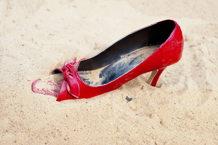 Red lady shoe in sand, concept of lost and found, outdoor closeup shotの写真素材