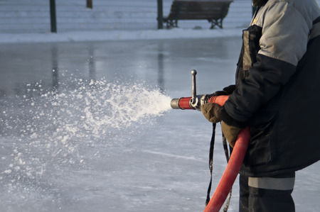 Man in uniform, holding a water hose, preparing an ice rink, outdoor winter sceneの写真素材