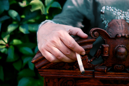 Female hand holding a cigarette, hand laid on a carved wooden retro back of the chair. Outdoor shot, concept of healthy lifestyleの写真素材