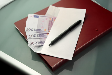 Open envelope with bribe in euro, with pen and documents waiting to be signed. Overhead shot with particular focusの写真素材