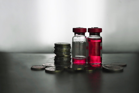 Close up of vials with red liquid and coins stacked, medicine expenses conceptの写真素材
