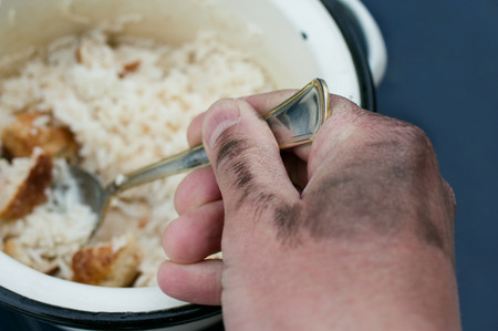 Dirty hand holding a spoon with food, horizontal shot with selective focus.の写真素材