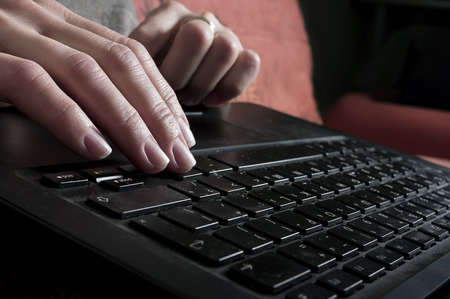 Closeup shot of female hands typing on a black laptop, indoor shot with blurred backgroundの写真素材