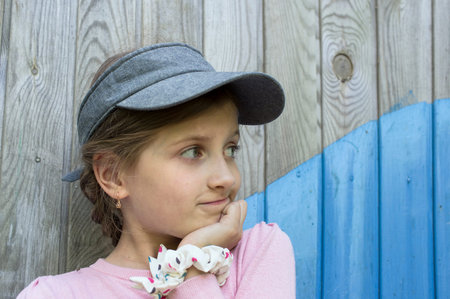 Girl of 7, little dreamer with a distant gaze, posing near a wooden wall