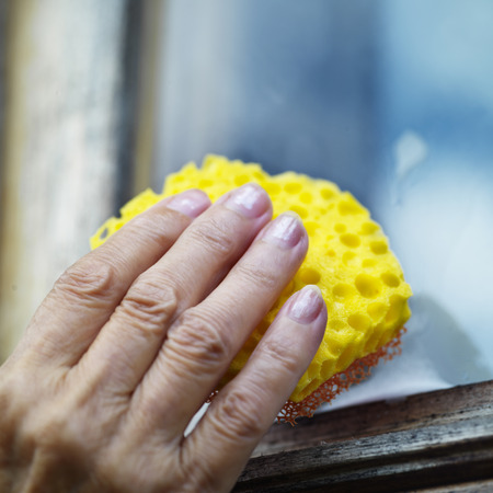 Female hand cleaning window by sponge and cleaning supplies, outdoor square shot with selective focusの写真素材