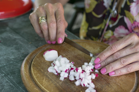 Female hand with manicure chopping horseradish for salad on a wooden kitchen tray, selective focus shotの写真素材