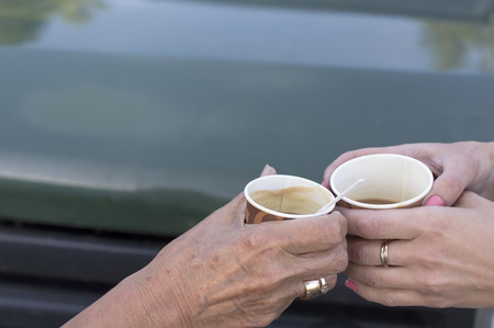 Two female hands, aged and young, holding cups of coffee in front of car, outdoor cropped shotの写真素材