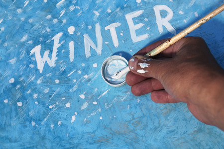 Male hand writing word Winter by artist brush on the blue painted boardの写真素材