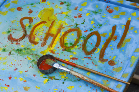 Closeup of the artist brushes laid on a desk painted in different colors, word School written in the image centerの写真素材