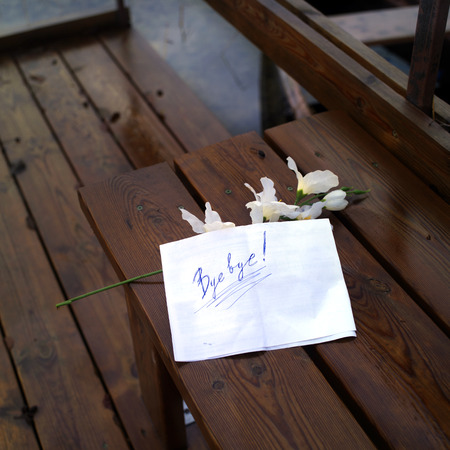 Farewell message laid on a wet bench next to flowers, concept of relationshipの写真素材