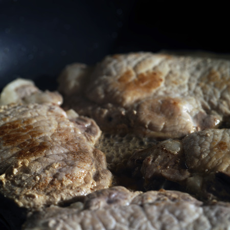 Cuts of beef cooking on a frying pan, macro shot with particular focusの写真素材