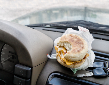 A bitten sandwich next to the ignition keys laid on a car dashboard, concept of having a coffee break while travel by carの写真素材