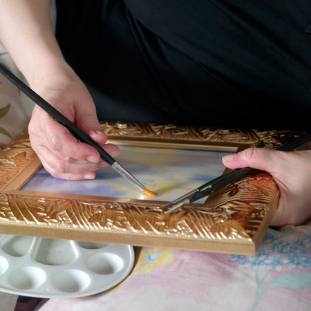 Female hands with paintbrushes, holding an artwork decorated in a golden frame, concept of the arts