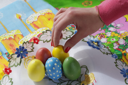 Female hands setting painted easter eggs on a table covered with colorful napkins
