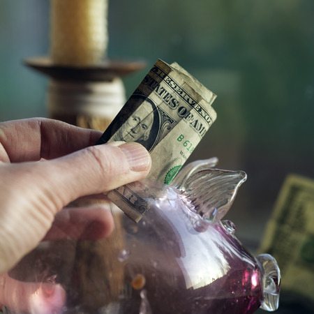Hand with a dollar bill taking or puting it into a pig saving pot, closeup indoor shot with selective focusの写真素材