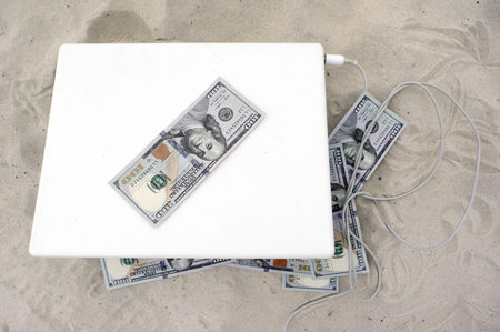 Overhead shot of a laptop and US dollars spread out around, day time shot with no peopleの写真素材