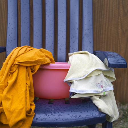 Various laundry in a pink washbowl, standing on the plastic chair, outdoor cropped shotの写真素材