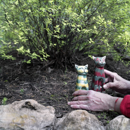 Female hands setting two statues of funny cats in her garden. Toned closeup shot with selective focusの写真素材