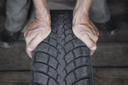 Hands of mechanic holding a tire with a winter tread in a garage, indoor front shot with selective focusの写真素材