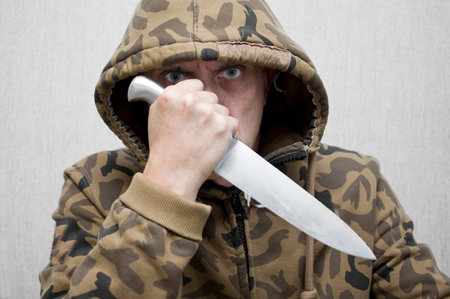 Man wearing camouflage and hood holding a big knife covering his face