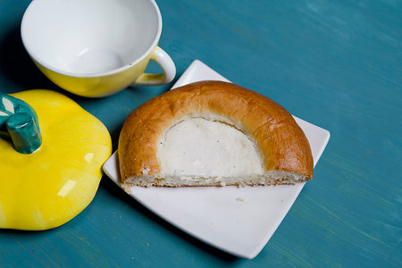 Half of a cheesecake on the white saucer next to tea pot and cup, angled studio shot