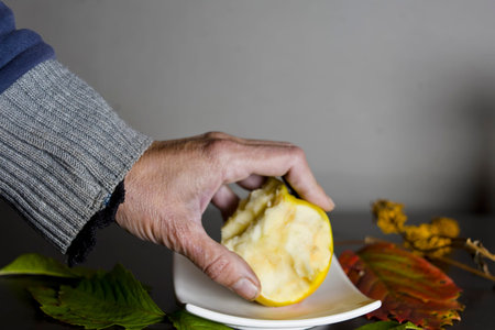 Female hand holding a bitten apple laid on the saucer, studio closeup shot with a shallow depth of...