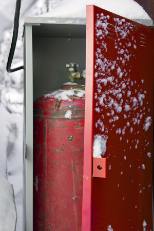 Gas bottle in a safe box standing outdoor, next to the house. Snow piles in the background.の写真素材