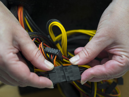 Female hands holding two connectors, bunch of cables in the background.の写真素材