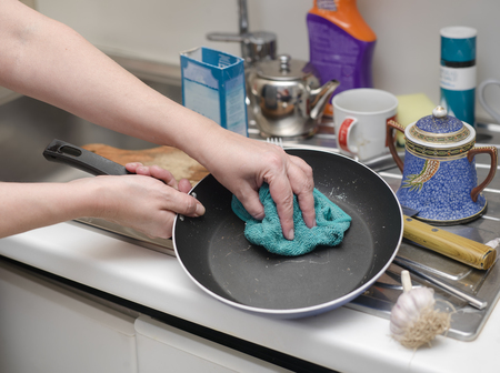Houseproud woman washing a frying pan in her messy kitchen, cropped selective focus shotの写真素材