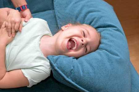 Extremely emotional portrait of a girl of 5 burst into laughter while another child tickling herの写真素材
