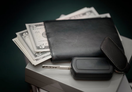 Car ignition key laid on a top of abstract passport or ID with some US currency in the backgroundの写真素材