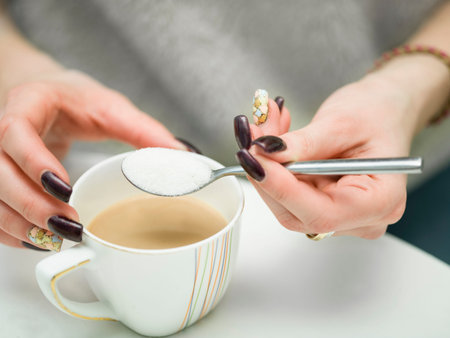 Female manicured hand about to put sugar into a coffee cup. Shallow depth of field macro shotの写真素材