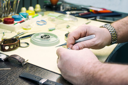 In a clock repair shop. Table with various precise equipment and hands of a service man. Filtered...