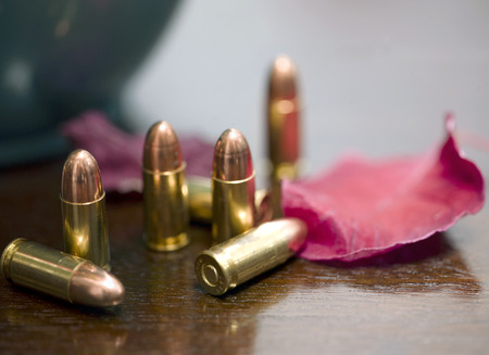 Bunch of 9 mm cartridges and a red leaf laid on a wooden table, shallow depth of field closeupの写真素材