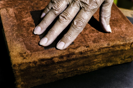 Old book with a red velvet cover and female hand about to open it, closeup filtered shotの写真素材