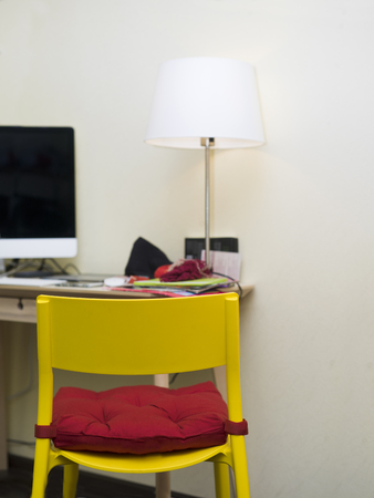 Yellow chair with red seat in focus and a desk with computer in the background, vertical indoor shotの写真素材