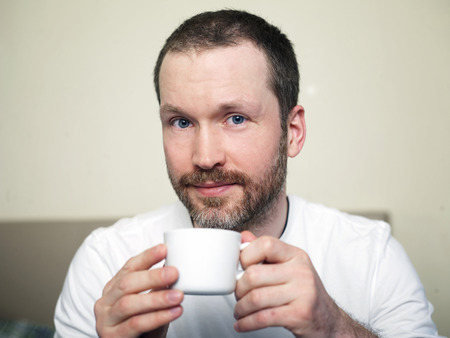 Mid aged man holding a cup of coffee or tea with a pleasant look on his face, indoors cropped shotの写真素材