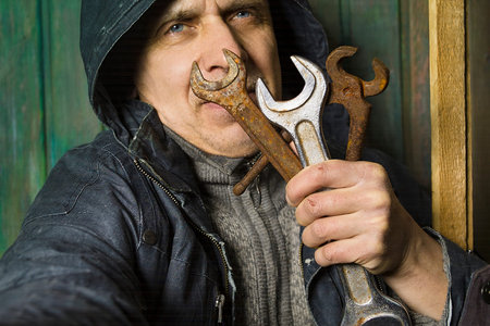 Worker wearing protective coat holding a bunch of hand tools in front of his face. Studio cropped portraitの写真素材