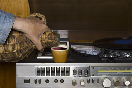 Hand with a bottle of alcohol next to the retro stereo vinyl player, front closeup shotの写真素材