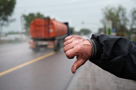 A male hand hitching a lift and a motorway with truck in the blurred backgroundの写真素材