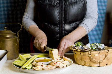 Female hands chopping cheese and vegetables on a kitchen table, interior shotの写真素材