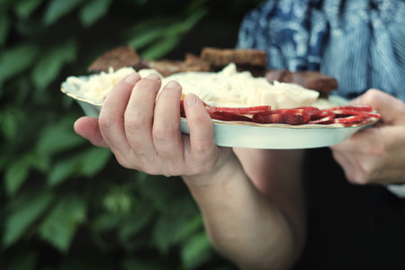 Female hands holding a plate with salami and cheese, green foliage in the background